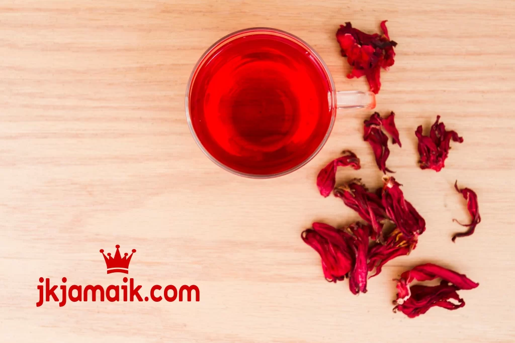 Una taza de té de hibisco con flores secas al lado.